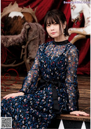 A woman sitting on a wooden floor wearing a white blouse and skirt.