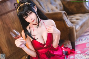 A woman in a red dress sitting on a chair holding a glass of wine.