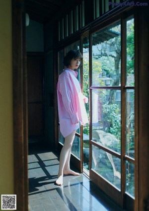 A woman looking out of a window with her hand on her chin.