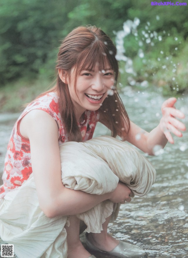 A woman in a red and white dress crouching down in a stream.