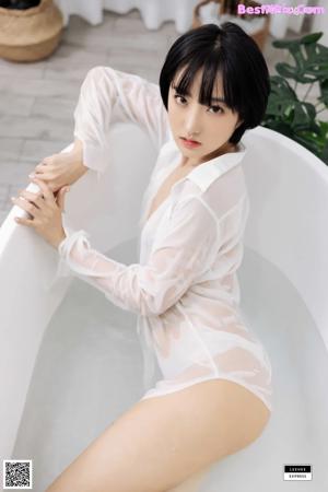 A woman in a white shirt is sitting on a bed.