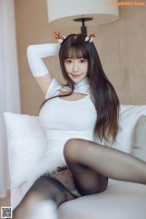A woman in a white dress posing on a white couch.