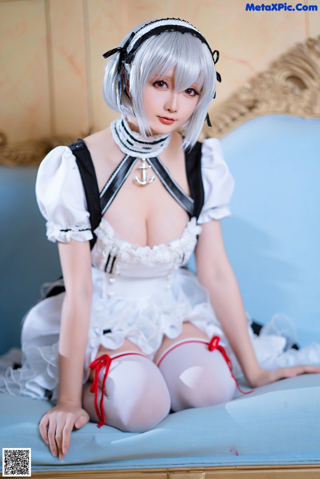 A woman in a maid outfit sitting on a bed.