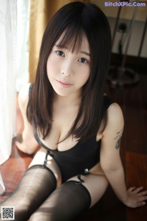 A woman in a black bodysuit and stockings posing for the camera.