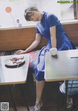 A woman in a blue dress holding a leaf in her hand.