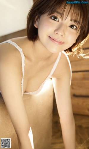 A woman in a white bra and blue panties sitting on a bed.