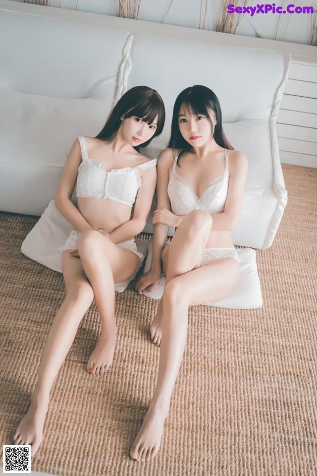 Two young women sitting on a white couch.